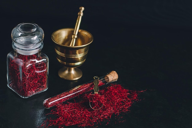 Foto rauwe biologische rode gedroogde saffraankruiden op houten ondergrond in vintage metalen messing vijzel met stamper glazen pot en buis