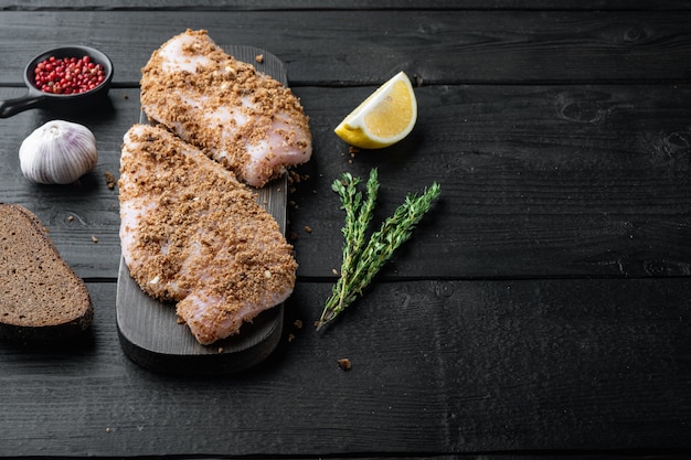 Rauwe crumbet-kipfilet met ingrediënten, op zwarte houten tafel met kopieerruimte