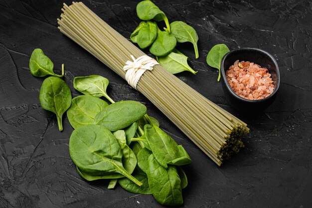 Rauwe droge groene spaghetti met spinazie set, op zwarte donkere stenen tafel achtergrond