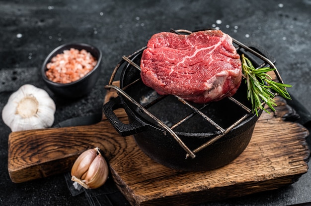 Rauwe filet mignon biefstuk op een grill met kruiden. Zwarte achtergrond. Bovenaanzicht.