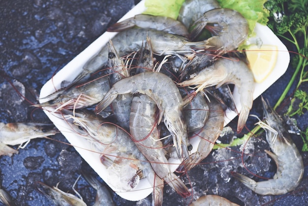 Rauwe garnalen op plaat plastic dienblad Verse garnalengarnalen voor het koken met kruiden citroen groentesalade sla op donkere achtergrond in het visrestaurant