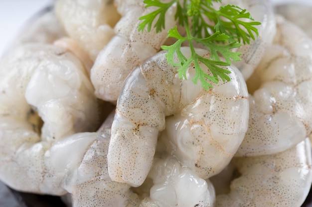 Rauwe gepelde garnalen of garnalen gerangschikt in een zwarte keramische kleine pot en gegarneerd met korianderblad dat klaar is om te koken op een witte gestructureerde achtergrond