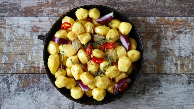 Rauwe geschilde aardappelen geheel in een pan met kruiden, kruiden en knoflook voor het bakken