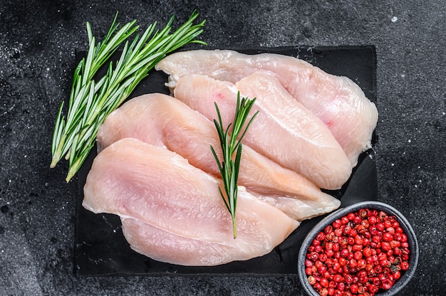 Rauwe gesneden kipfilet steaks op een marmeren bord. zwarte achtergrond. bovenaanzicht.