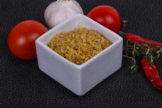 Rauwe gouden bulgur in de kom met tomaten en knoflook