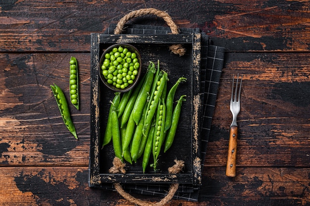 Rauwe groene erwt peulen in een houten dienblad. Donkere houten achtergrond. Bovenaanzicht.