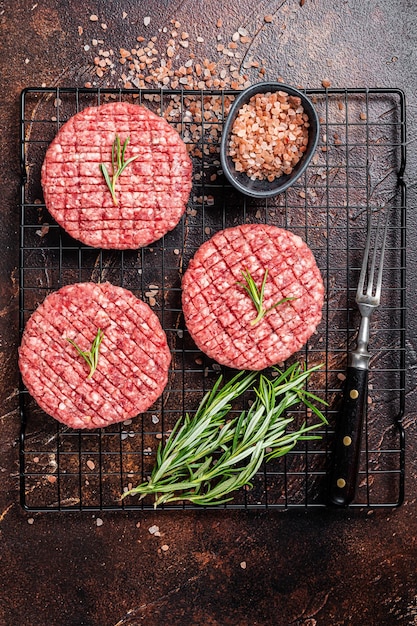 Rauwe hamburgerkotelet van rundvlees met kruiden en rozemarijn klaar om te koken donkere achtergrond bovenaanzicht