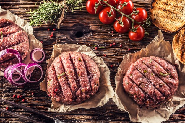 Rauwe hamburgers op houten tafel met ui tomaten kruiden en specerijen.