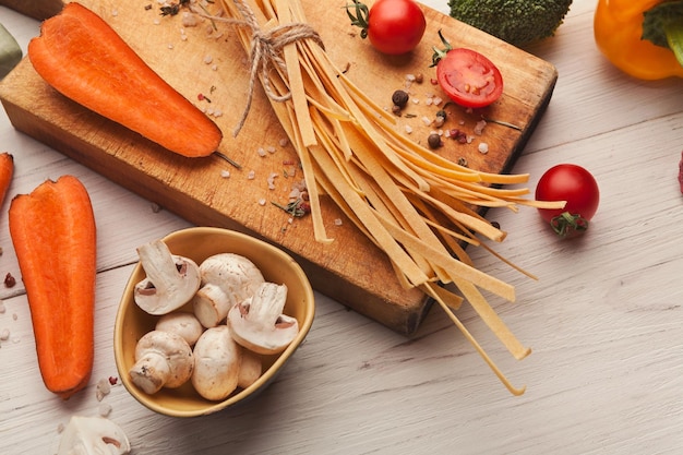 Rauwe handgemaakte oranje tagliatelle met wortelsap, tomaten, broccoli, champignons en kruiden op witte houten tafel. Pasta achtergrond koken, ruimte kopiëren