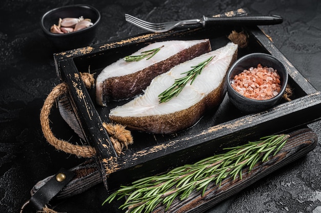 Foto rauwe heilbot vis steak in houten dienblad met kruiden. zwarte achtergrond. bovenaanzicht.