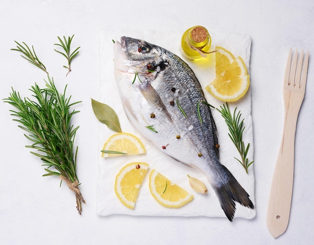 Rauwe hele dorado vis op wit bord en kruiden voor het koken bovenaanzicht op witte tafel