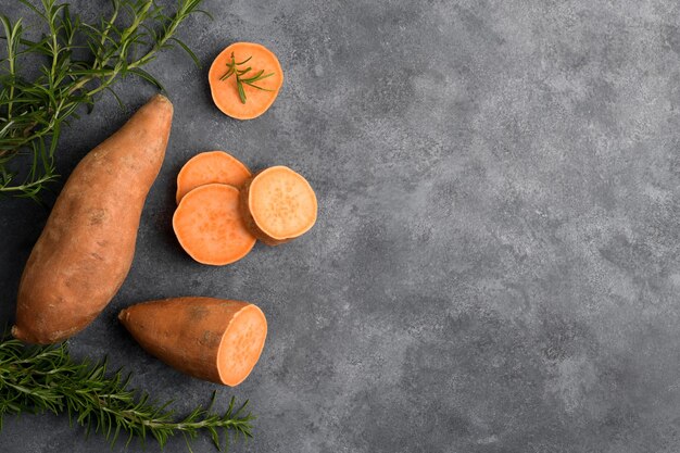 Rauwe hele oranje zoete aardappel en plakjes batat met verse rozemarijn op grijze stenen tafelachtergrond