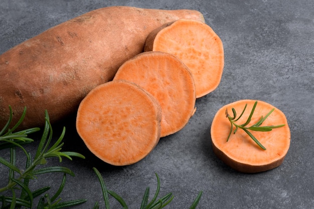 Rauwe hele oranje zoete aardappel en plakjes batatas met verse rozemarijn op grijze stenen tafelachtergrond