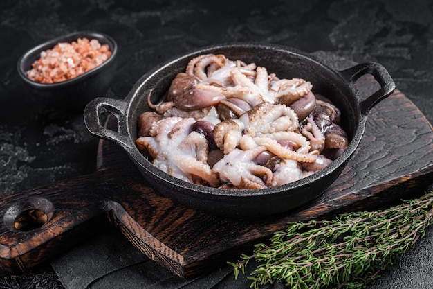 Rauwe jonge baby-octopus in een koekenpan klaar om te koken. Zwarte achtergrond. Bovenaanzicht.