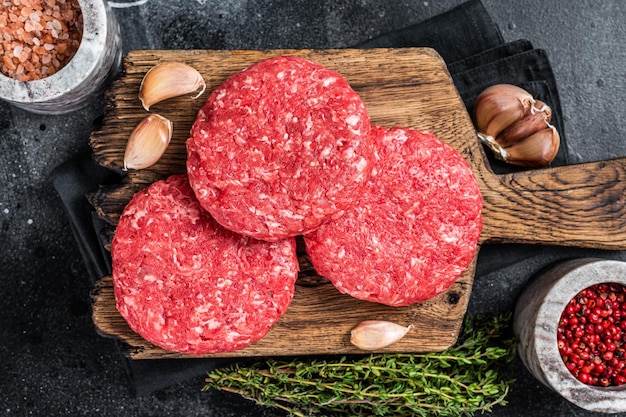 Rauwe kalfshamburgerpasteitjes met kruiden en specerijen. Zwarte achtergrond. Bovenaanzicht.