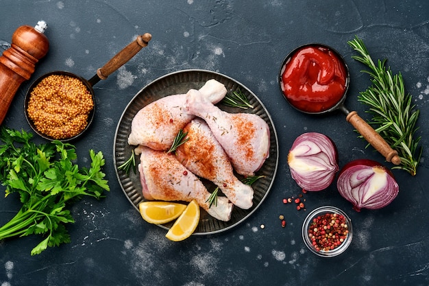 rauwe kip drumsticks met ingrediënten voor het koken op een zwarte stenen achtergrond. voedsel achtergrond,