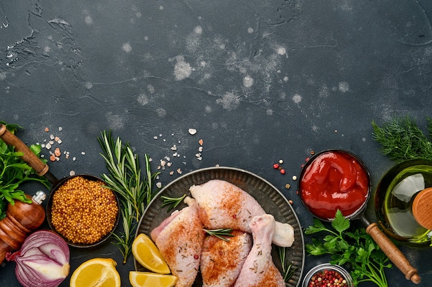 Rauwe kip drumsticks met ingrediënten voor het koken op een zwarte stenen ondergrond. Bovenaanzicht.