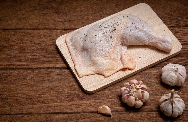 Rauwe kippendijen en knoflookpeper op een houten lijst