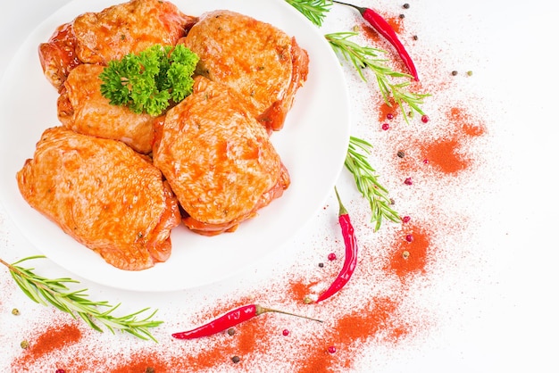 Rauwe kippendijen gemarineerd in rode saus op een wit bord met verse rozemarijn en rode peper