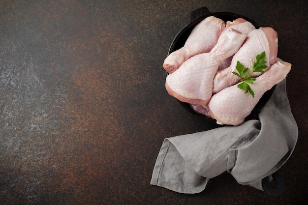 Rauwe kippenpoten op een gietijzeren pot met kruiden en specerijen op een donkere beton of steen bereid om te koken.