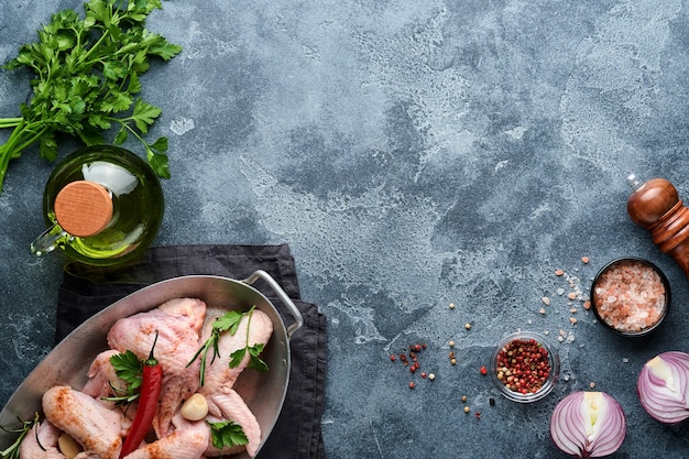 Rauwe kippenvleugels in metalen pan of kom met kruiden en ingrediënten voor het koken op donkergrijze leisteen, steen of betonnen ondergrond. rauw vlees met kruiden aan zwarte tafel. bovenaanzicht. bespotten.