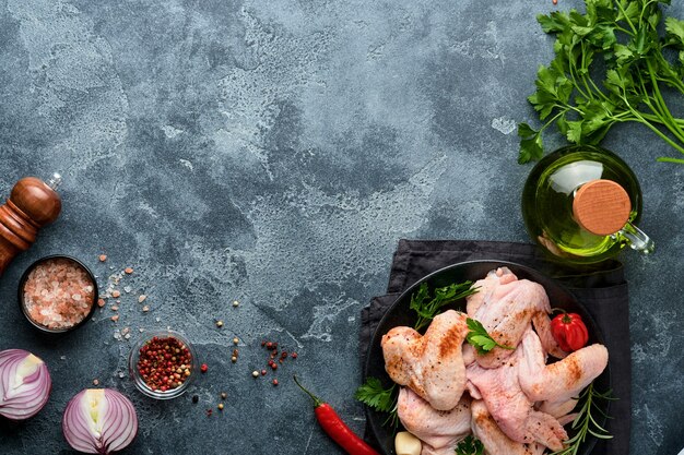 Rauwe kippenvleugels in metalen pan of kom met kruiden en ingrediënten voor het koken op donkergrijze leisteen, steen of betonnen ondergrond. rauw vlees met kruiden aan zwarte tafel. bovenaanzicht. bespotten.