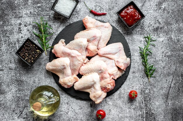 Rauwe kippenvleugels op een zwarte plaat met ingrediënten om te koken.