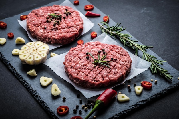 Rauwe kotelet van gehakt met ingrediënten op een donkere kookachtergrond