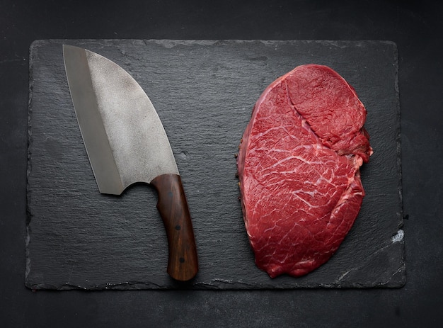 Rauwe ossenhaas ligt op een snijplank en kruiden om te koken op een zwart tafelblad