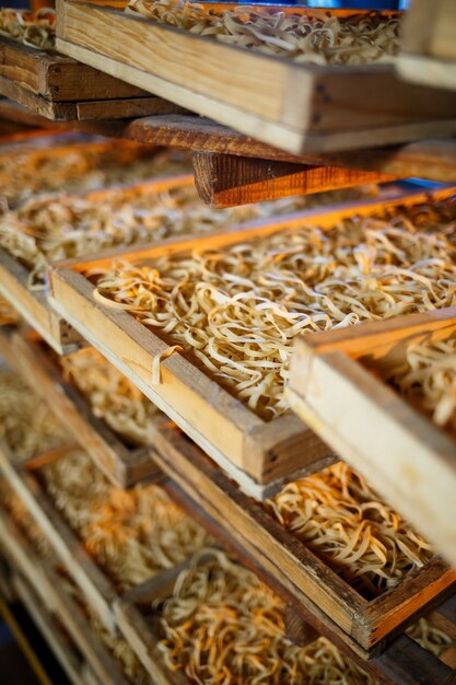 Rauwe pasta, spaghetti en noedels liggen op een plank in een houten kist in de fabriek. Pasta maken. Detailopname. horizontaal