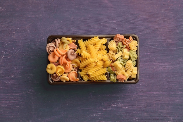 Rauwe pasta van verschillende soorten vormen en kleuren liggen in een doos in het midden van het frame op een gekleurde