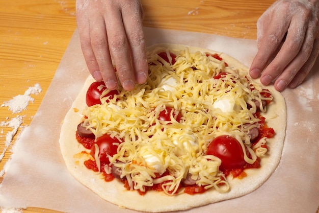 Rauwe pizza op bakpapier op de houten tafel Bereiding van zelfgemaakte ongekookte kaaspizza met tomaat