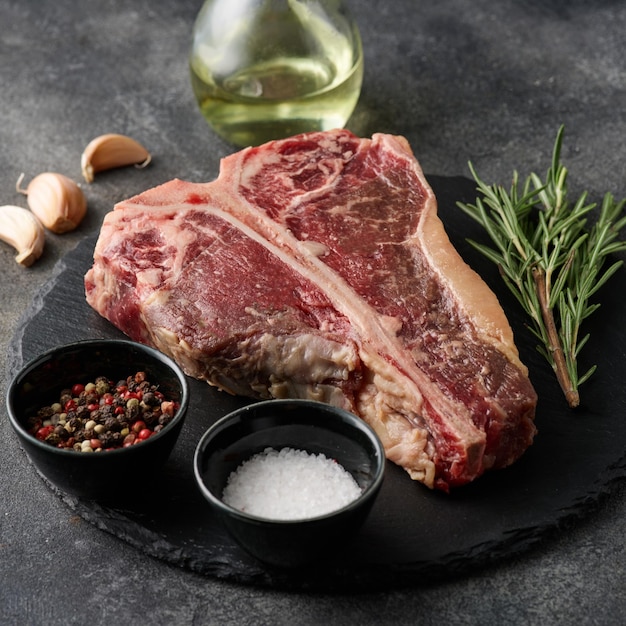 Rauwe porterhouse steak met kruiden op een donkergrijze tafel Rauw vers rundvlees Tbone steak