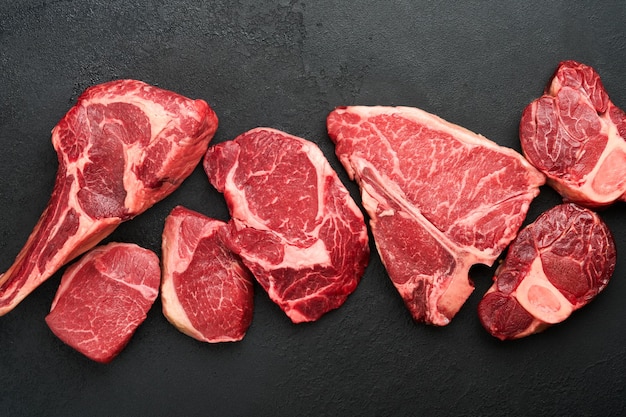 Rauwe prime steaks Verscheidenheid aan verse black angus prime vlees steaks Tbone New York Ribeye Striploin Tomahawk snijplank op zwarte of donkere achtergrond Set van verschillende klassieke steaks Bovenaanzicht