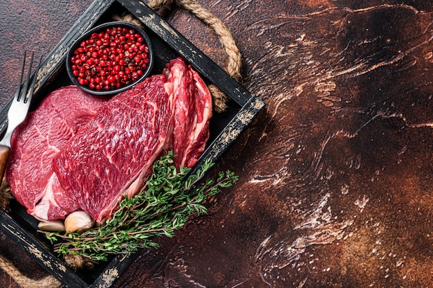 Rauwe rib eye biefstuk in een houten dienblad met kruiden. Donkere achtergrond. Bovenaanzicht. Ruimte kopiëren.