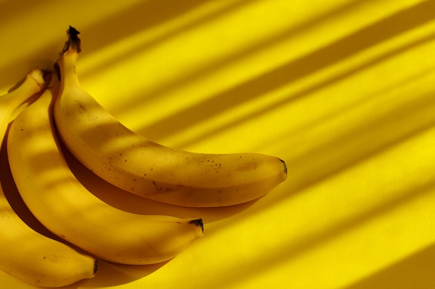 Foto rauwe rijpe zoete biologische bananen op geel met tropische schaduwen.