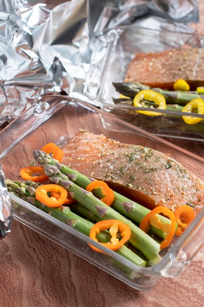 Foto rauwe rode zalm met zout en specerijen met groene asperges en paprika in een schotel