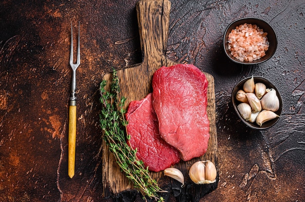 Rauwe rump beef vlees steaks op een houten bord van de slager. Donkere achtergrond. Bovenaanzicht.