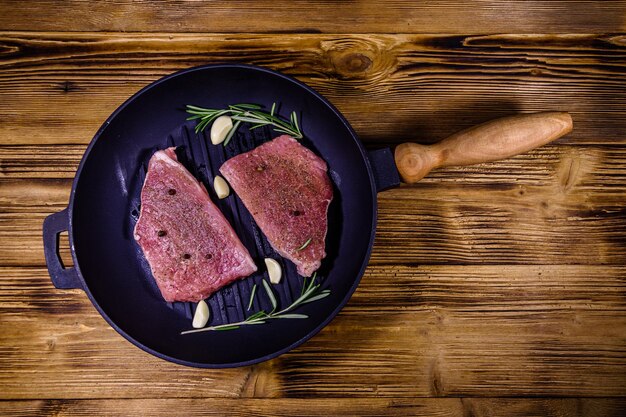 Rauwe steaks met knoflook, rozemarijn en kruiden in een gietijzeren grillpan. Bovenaanzicht