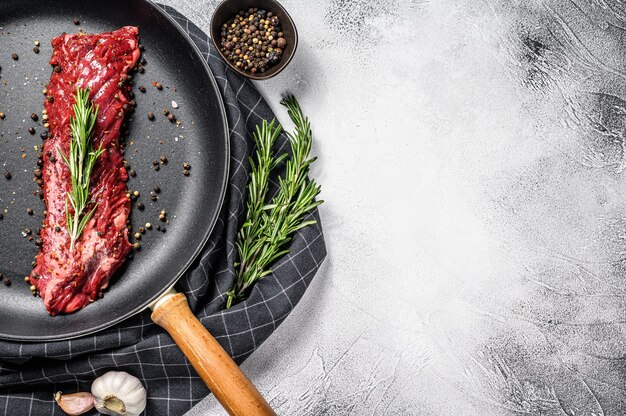 Rauwe strip vegas steak in een pan met ingrediënten koken. grijze achtergrond