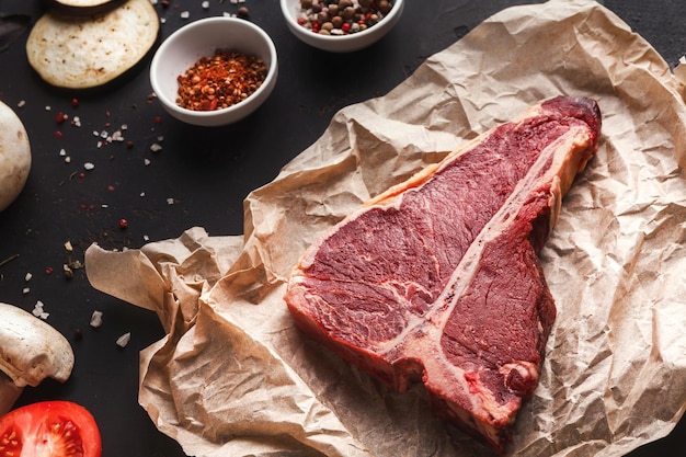 Rauwe t-bone steak op ambachtelijk papier op donkere achtergrond. Prime vlees op zwarte tafel met kruiden, kopieer ruimte