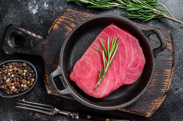 Rauwe tonijnfilet met rozemarijn in een pan. Zwarte achtergrond. Bovenaanzicht.