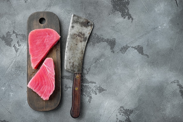 Rauwe tonijnsteak set, op houten snijplank, en oud slagersmes, op grijze steen