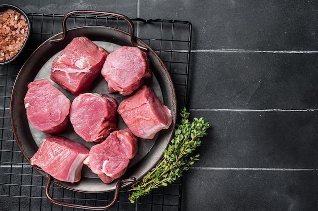 Rauwe varkenshaas medaillons steaks op een keukenblad met tijm en zeezout Zwarte achtergrond Bovenaanzicht Kopieer ruimte