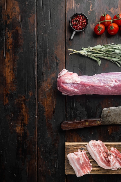 Rauwe varkenslende met ingrediënten en kruiden voor het bakken, salie, aardappel set met oud slagersmes, op oude donkere houten tafel, bovenaanzicht plat gelegd