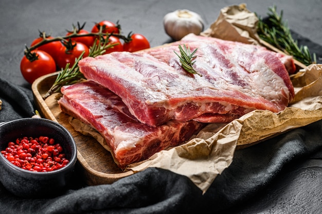 Rauwe varkensribbetjes met ingrediënten voor het koken van rozemarijn en knoflook in een houten kom.