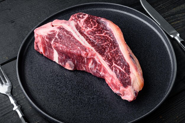 Rauwe verse beef tbone steak drya leeftijd gesneden op plaat op zwarte houten tafel achtergrond met kopieerruimte voor tekst