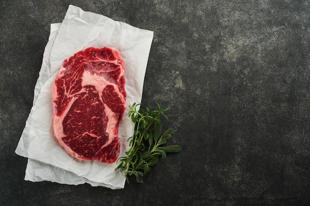 Rauwe verse ribeye steak of Ribeye steak Rauw vers gemarmerd vlees Ribeye Black Angus en kruiden peper rozemarijn tijm en zout op oude houten rustieke achtergrond Bovenaanzicht en kopie ruimte