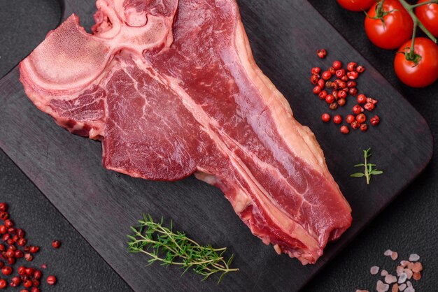 Rauwe verse sappige beef tbone steak met zoute specerijen en kruiden op een donkere betonnen achtergrond