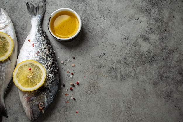 Rauwe verse vis dorado met partjes citroen, olijfolie en kruiden op grijze betonnen ondergrond klaar om te koken. hele ongekookte vis en ingrediënten voor een gezond diner of dieetmaaltijd, ruimte voor tekst